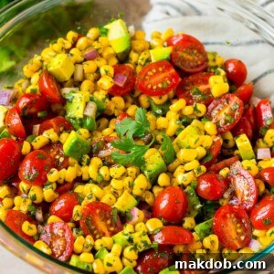 A bowl of corn salad with avocado and tomato, all tossed in a lime dressing.