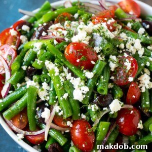 A bowl of green bean salad made with feta cheese, tomatoes, red onion and kalamata olives.