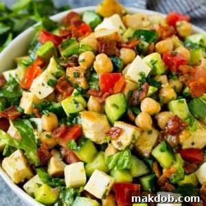 A bowl of chopped salad made with chicken, lettuce, tomato, cucumber, bacon and chickpeas.