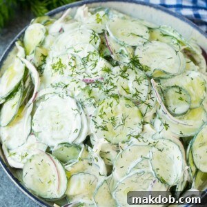 Creamy cucumber salad with red onion and dill, topped with fresh herbs for garnish.
