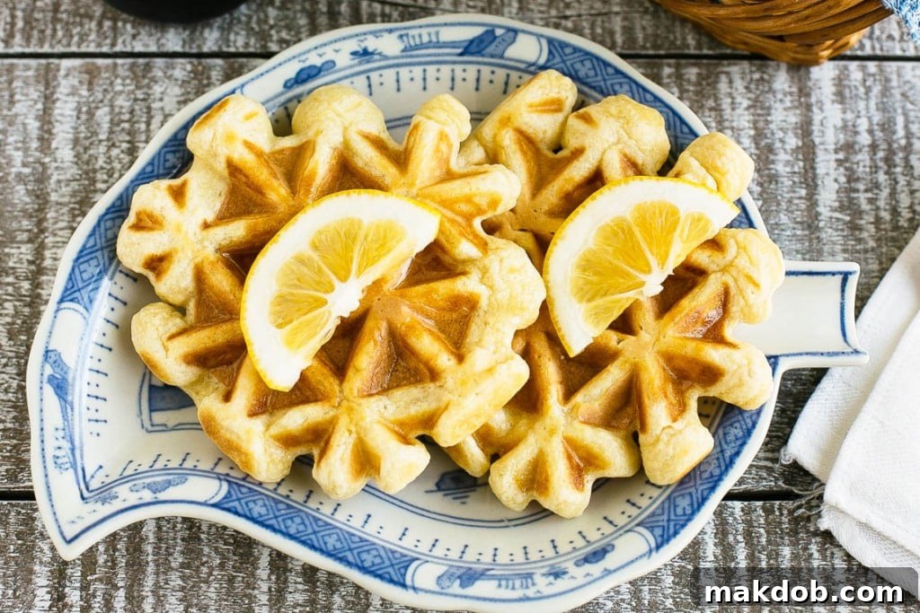 A large stack of golden brown lemon sour cream waffles on a plate, ready to be served.