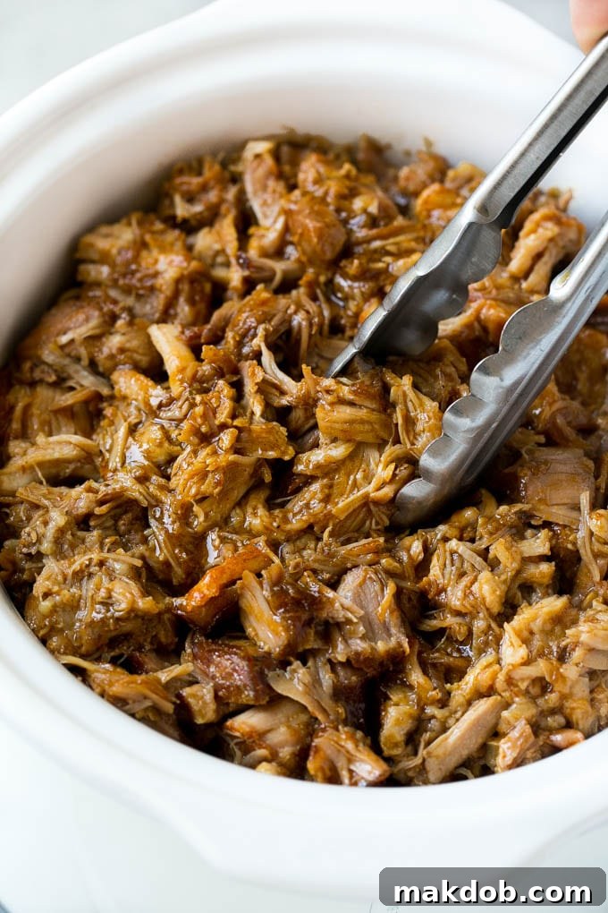 Slow Cooker Pulled Pork: Shredding Tender Pork in a Crockpot for Sandwiches. #pulledpork #crockpotcooking #easyrecipe Tender pulled pork in a slow cooker, being shredded with tongs.