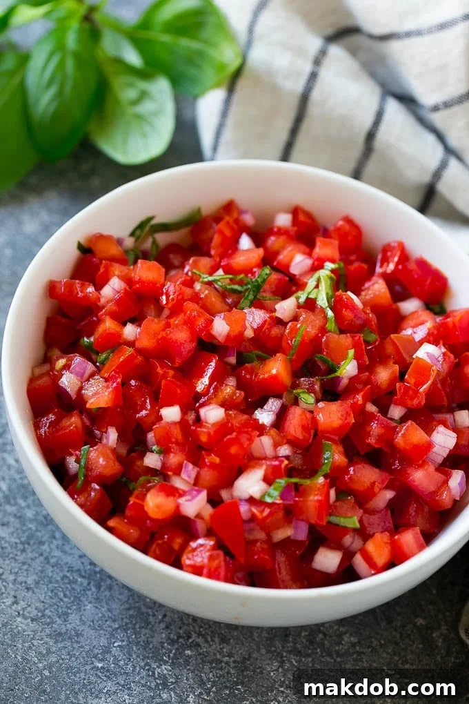 A vibrant bowl of fresh tomato bruschetta topping, featuring diced red tomatoes, chopped green basil, and minced red onion, ready to be served.