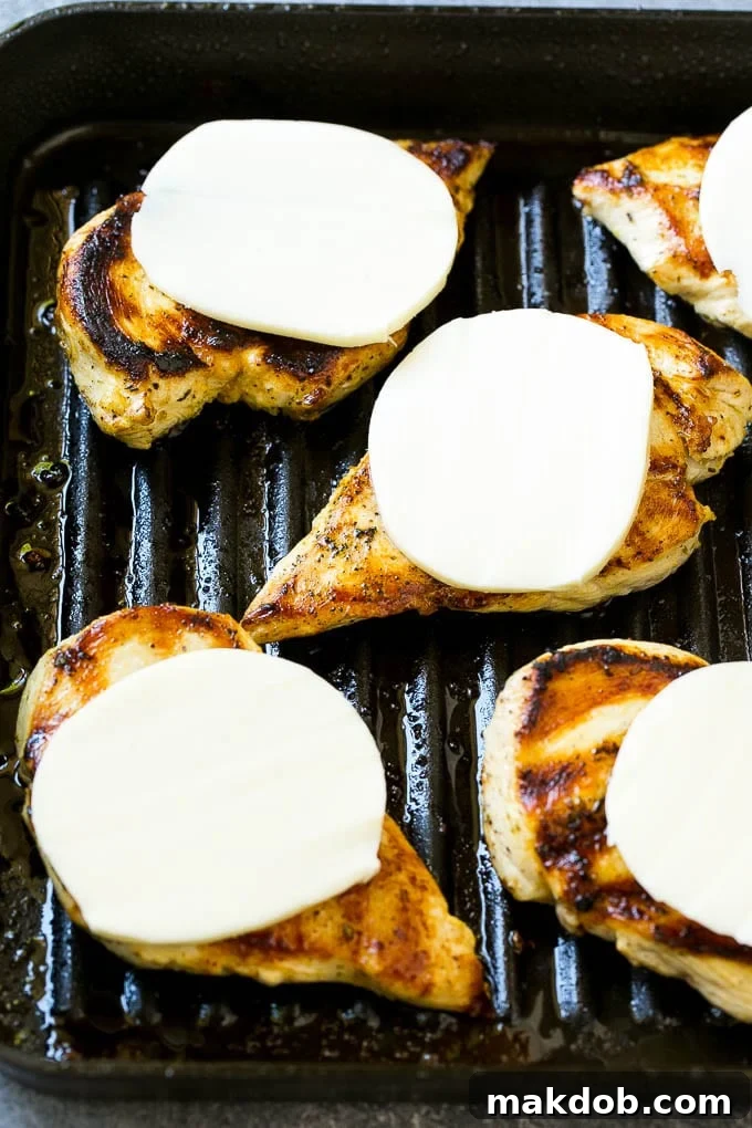 Four grilled chicken breasts, each topped with a melting slice of mozzarella cheese, resting on a grill pan.