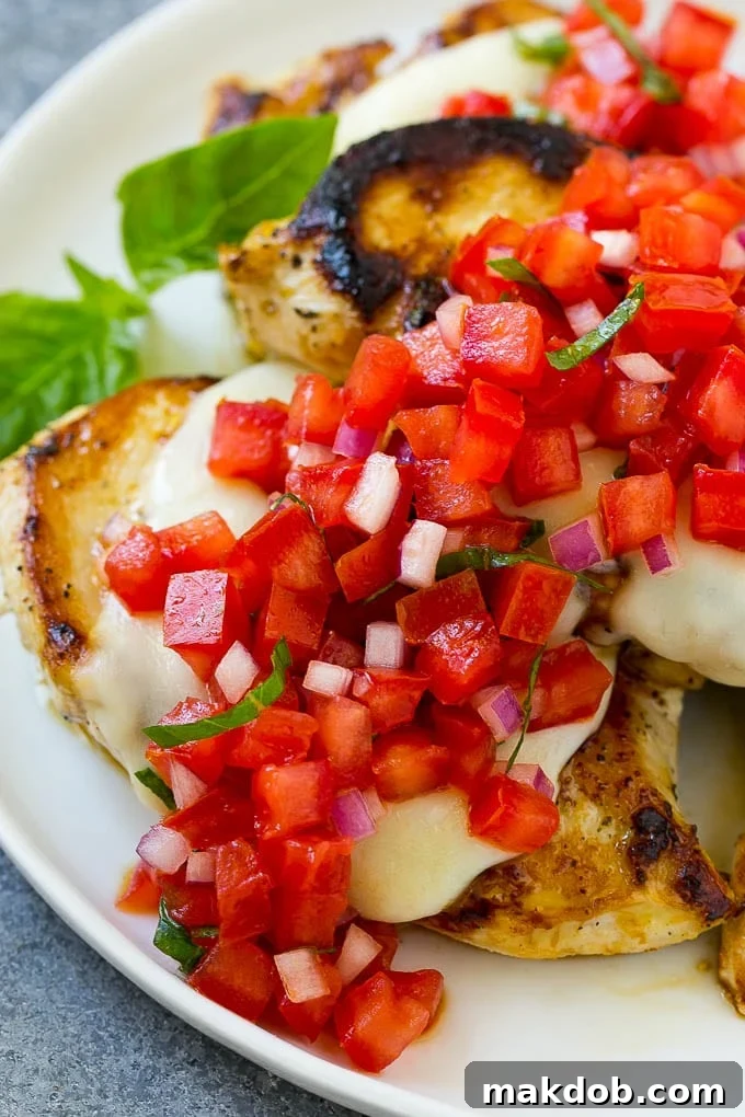 A close-up of grilled chicken topped with melted mozzarella cheese and a generous spoonful of fresh tomato bruschetta.