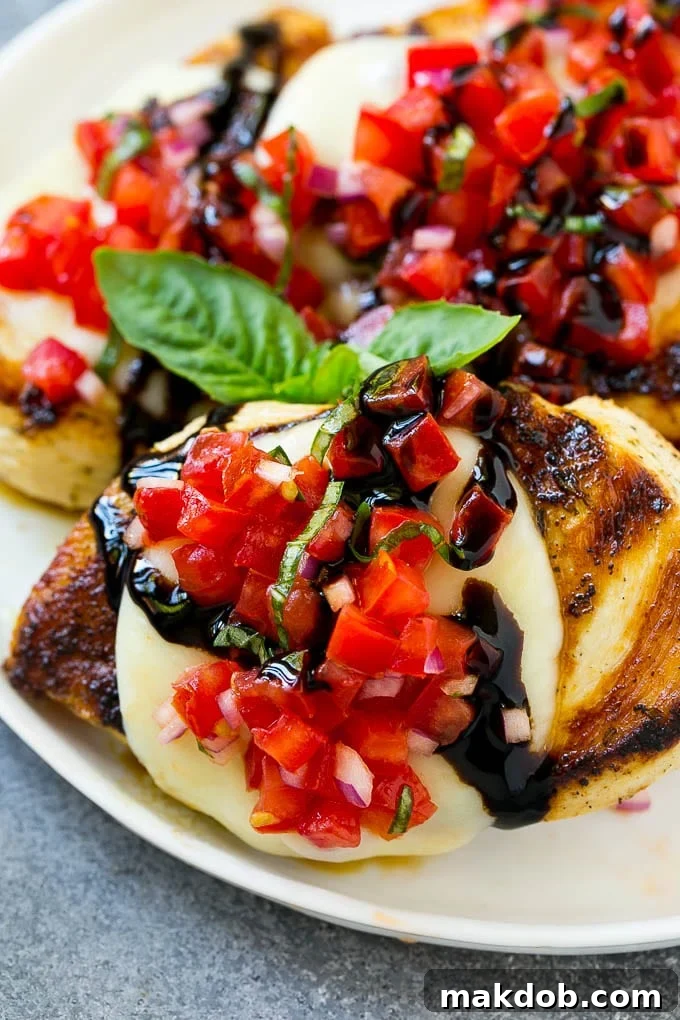 A beautifully plated bruschetta chicken dish, showcasing grilled chicken topped with melted mozzarella, a vibrant heap of tomato basil bruschetta, and a rich balsamic glaze drizzle, garnished with fresh basil.