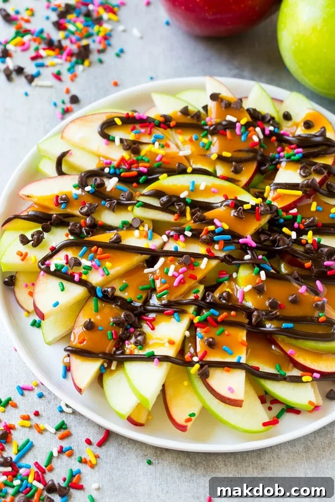 A beautifully arranged plate of sliced apple nachos, generously coated with glistening caramel and chocolate sauces, adorned with vibrant rainbow sprinkles and an assortment of mini chocolate chips, ready to be enjoyed.