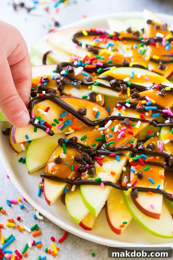 A close-up shot of a plate of caramel apple nachos, with a hand delicately reaching in to grab a perfectly topped apple slice.
