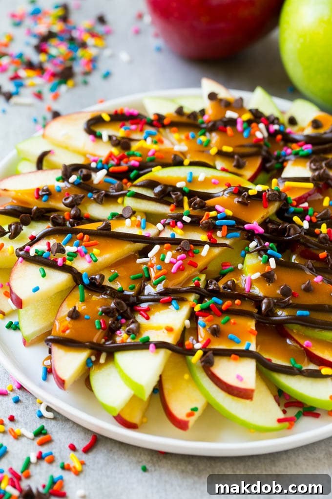 A plate of red and green sliced apples drizzled with caramel and chocolate, then topped with rainbow sprinkles and chocolate chips.