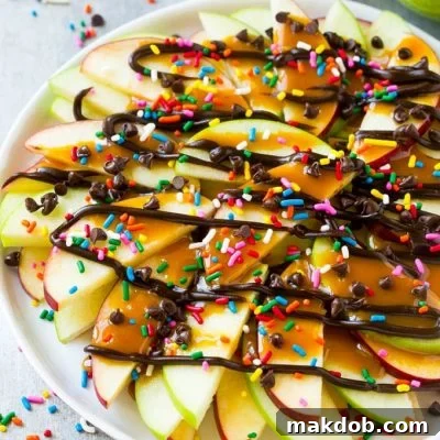 A plate of sliced apples topped with caramel and chocolate sauces, rainbow sprinkles and mini chocolate chips