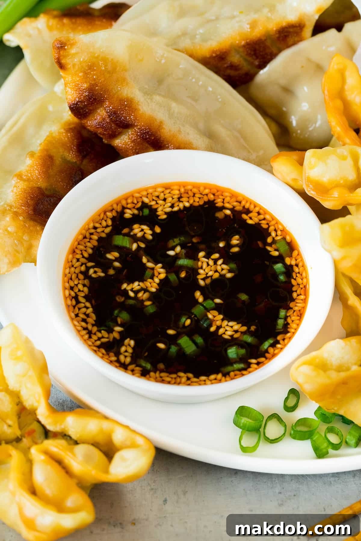 A bowl of dumpling sauce surrounded by dumplings and wontons.