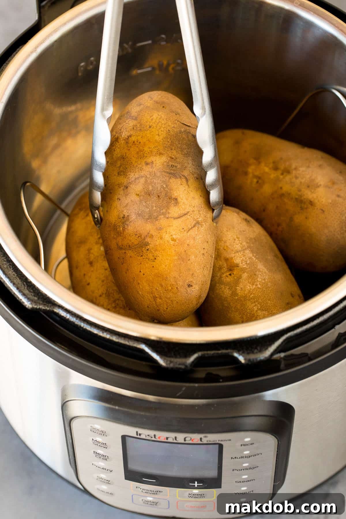 Tongs carefully removing a fluffy baked potato from an Instant Pot, ready for toppings.