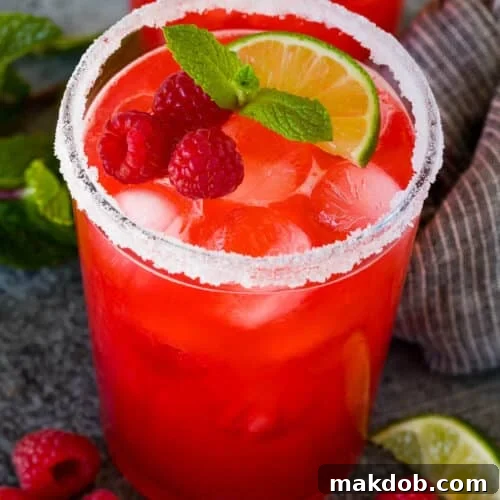 Glasses of raspberry margarita garnished with berries, mint and lime.