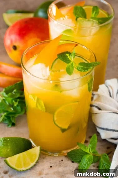 Glasses of mango mojito with garnishes of mint, limes and mango slices.