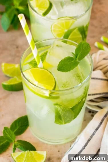 A cup of mojito mocktail garnished with limes and mint, with a green striped straw.
