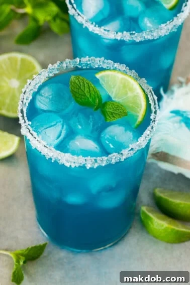 Two cups of blue margarita with a sugared rim and lime wedge for garnish.